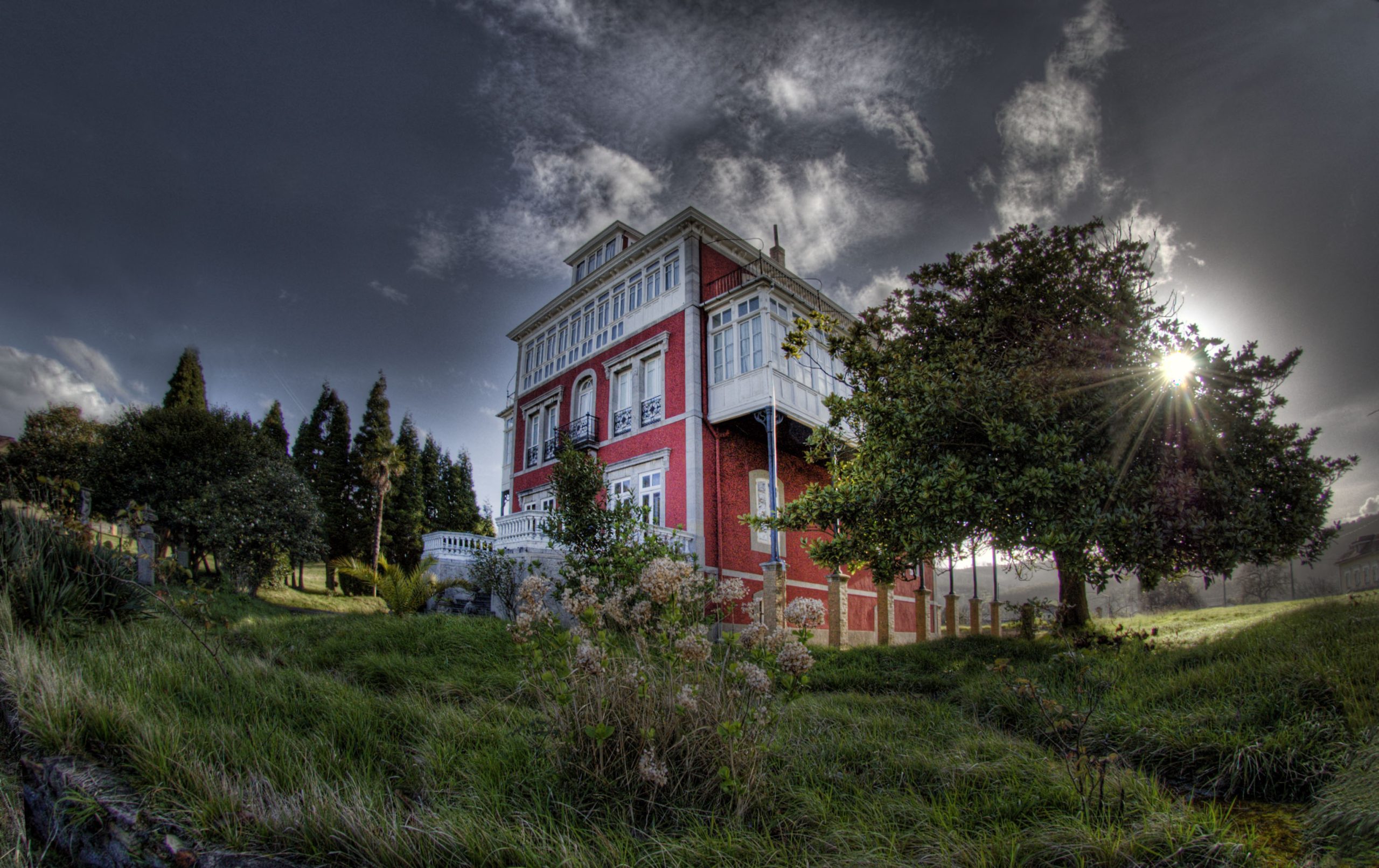 Casa de Somao con fachada rojiza, galerías blancas y árboles en su finca
