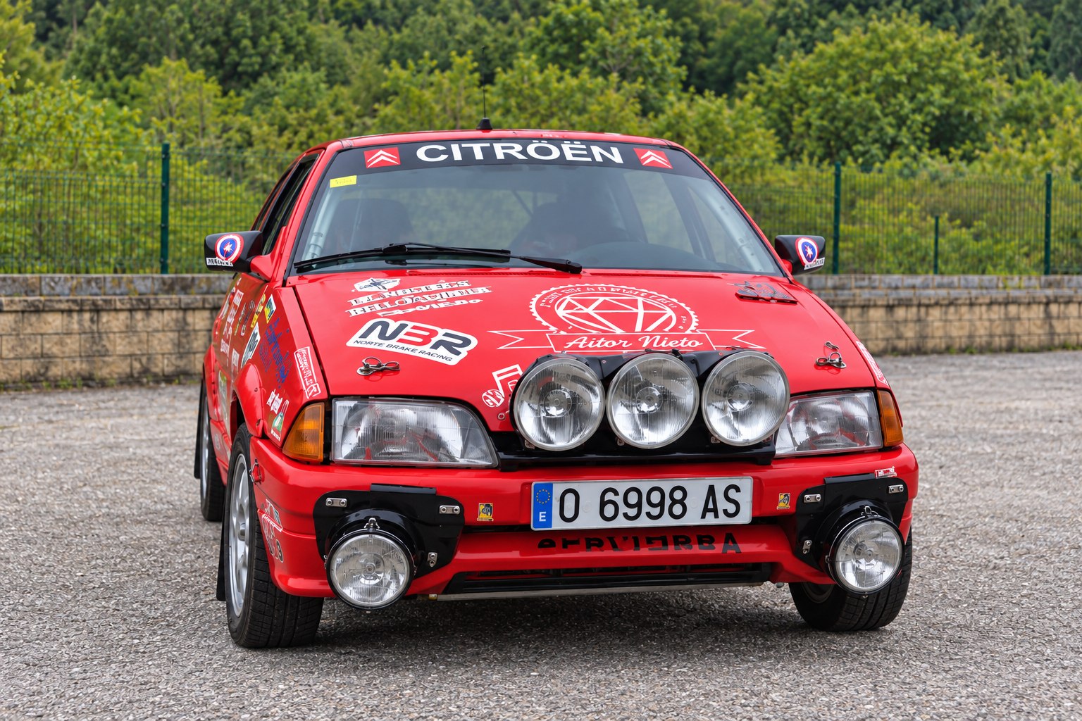 Vista frontal de un Citroën AX rojo de rally, adaptada a partir de la fotografía del cartel de Vanesa Martínez